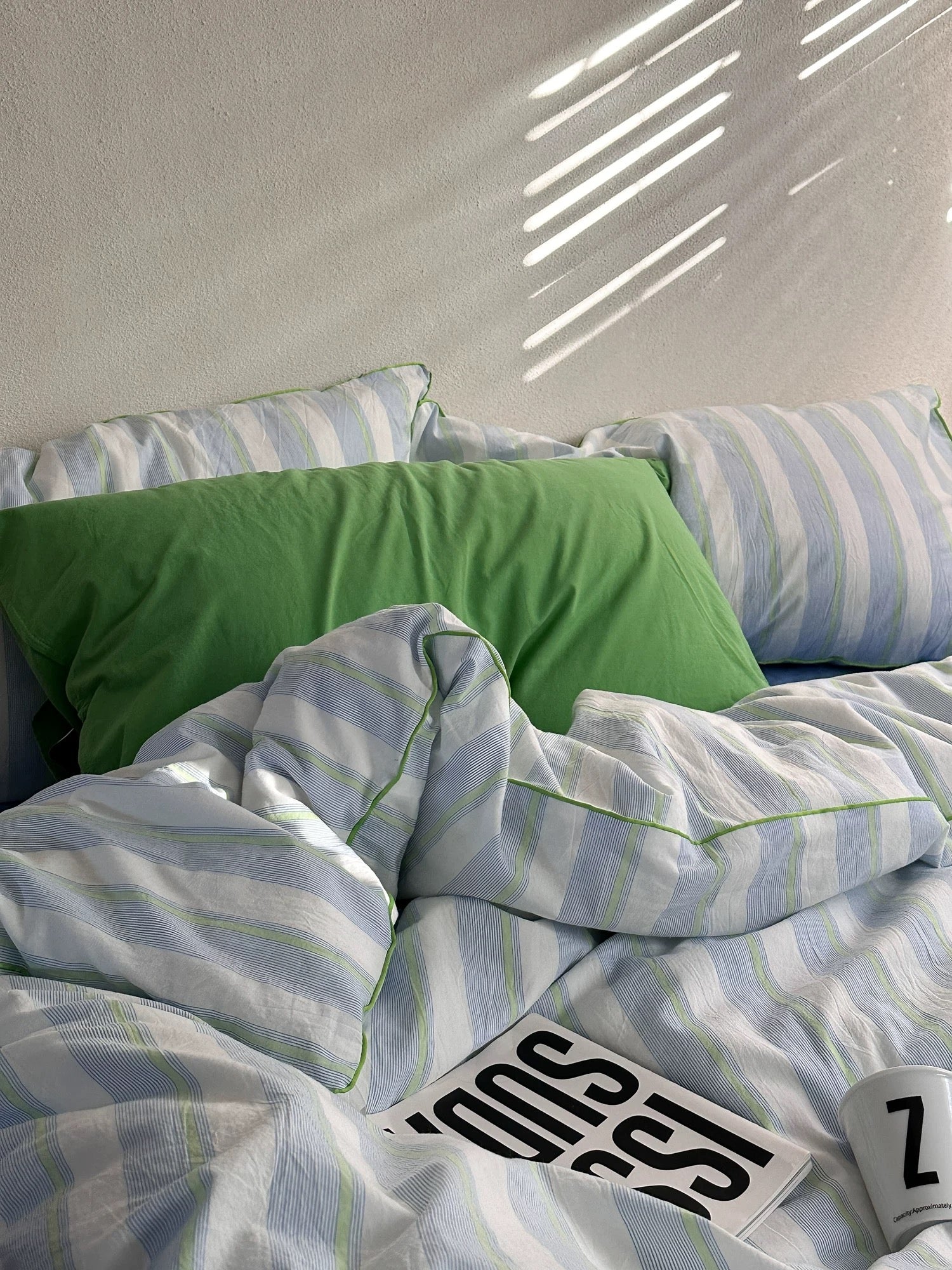 Striped bedding with a green pillow on a bed, featuring the brand 'Sass'.