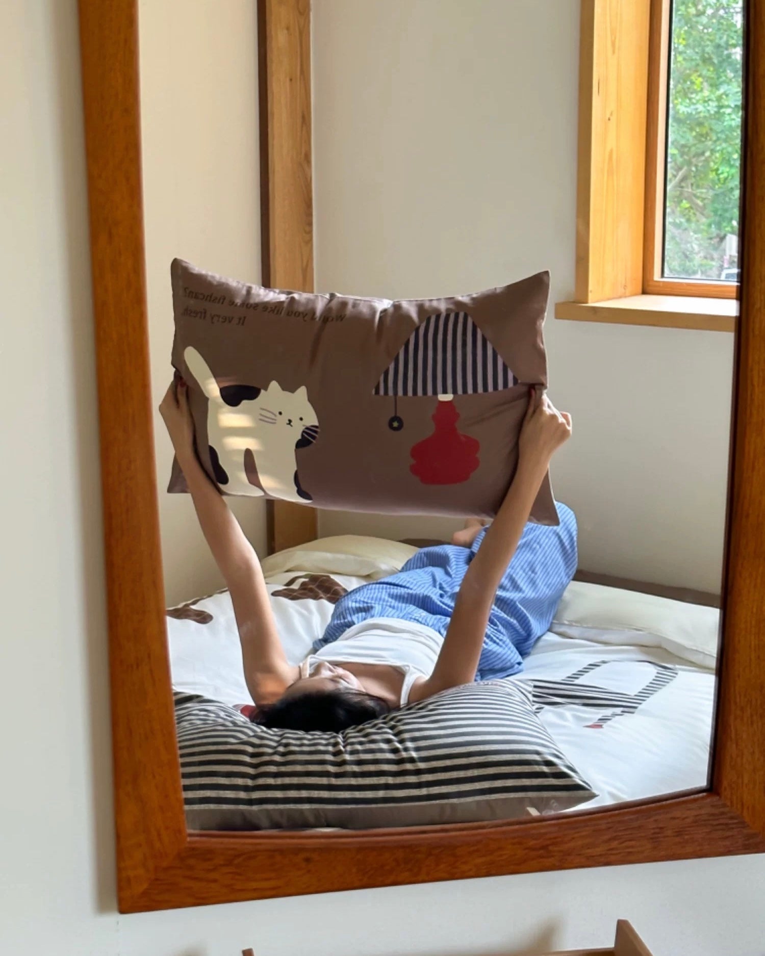 Person lying on a bed with cartoon pillow, reflected in a mirror.