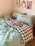 Bed with checkered blanket, green pillows, and teddy bear in a cozy bedroom setting.