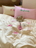 Bed with pink checkered pillow and teddy bear, featuring decorative elements on the bedding.