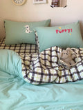 Bed with green bedding, plaid blanket, and pillows with dog and 'Puppy?' design.