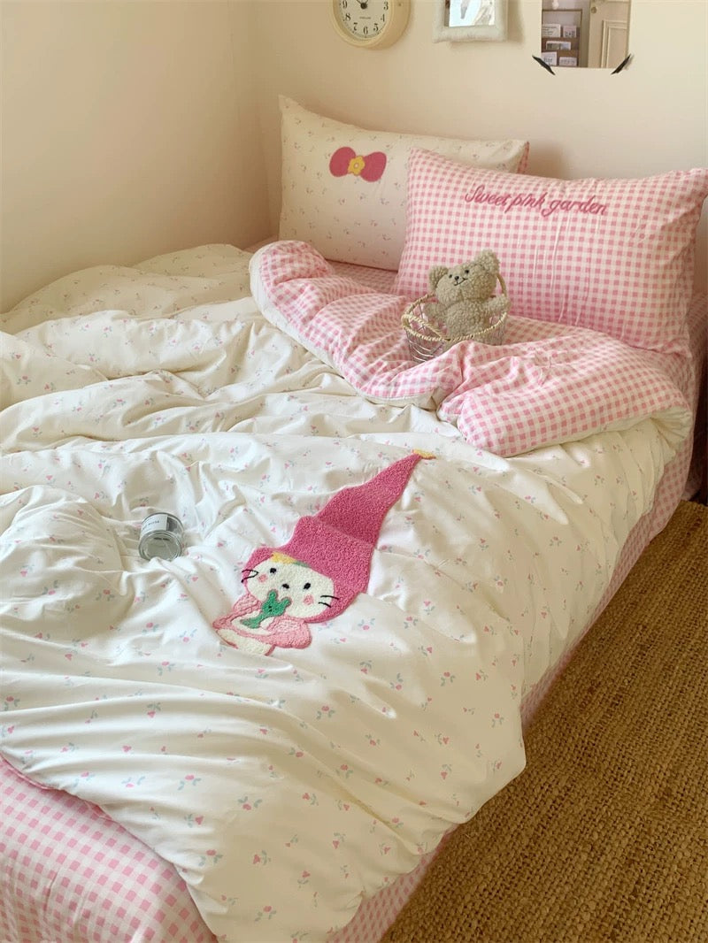 Children's bedroom with pink and white bedding featuring a gnome design, surrounded by decorative pillows and a teddy bear.