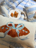 Decorative pillow with a croissant design on a bed with matching bedding.