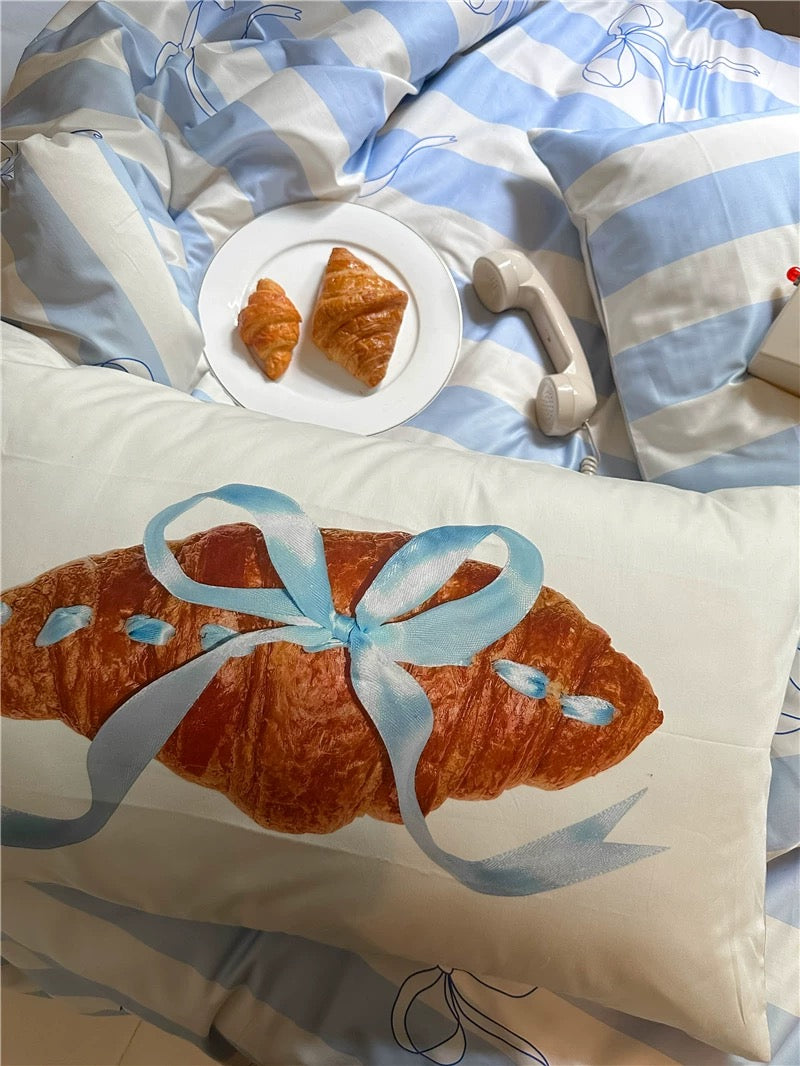 Decorative pillow with a croissant design on a bed with matching bedding.
