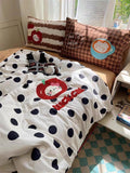 Polka dot blanket with cartoon design on a bed with decorative pillows.