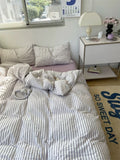 Bedroom with striped bedding, pillows, and a nightstand with a lamp.