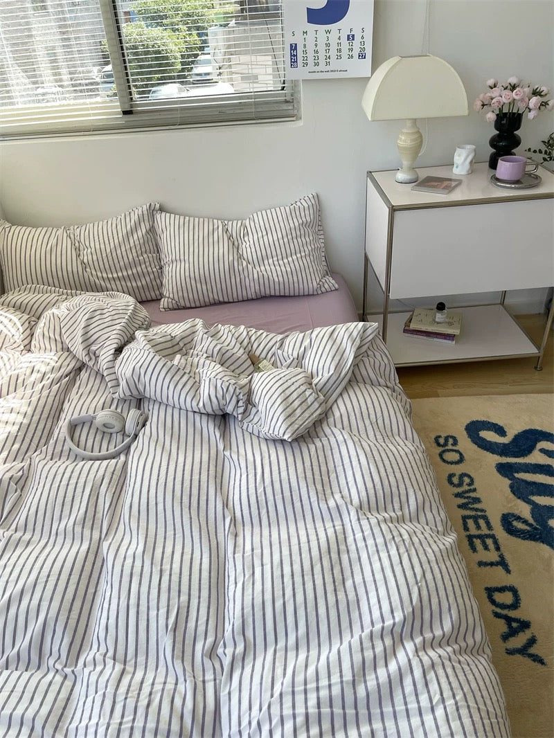Bedroom with striped bedding, pillows, and a nightstand with a lamp.