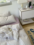 Bedroom with striped bedding and a nightstand with a lamp and decor items.