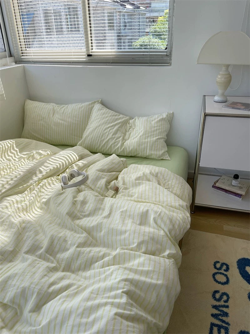 Bedroom with a bed covered in white bedding, a nightstand with a lamp, and a window with blinds.