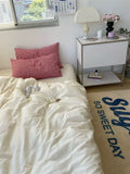 Bedroom with white bedding, red pillows, and a nightstand with a lamp.
