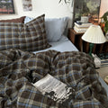 Plaid blanket and pillows on a bed with a lamp and books in the background