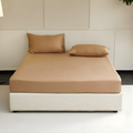 Beige bedspread and pillows on a white bed in a minimalistic room.