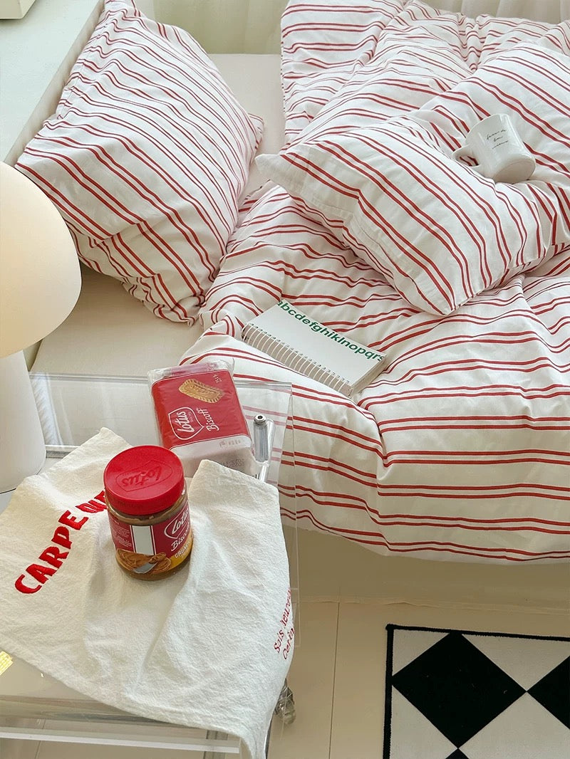 Striped bedding with a visible brand name on a bed, next to a plastic bag and jar on a surface.