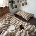 Bed with striped bedding and a book, mug, and plant on top in a cozy room.