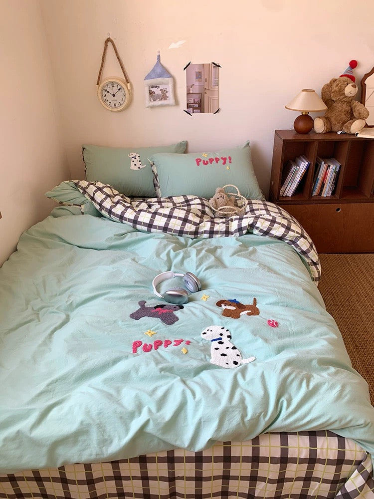 Bed with light blue bedding featuring dog illustrations, green pillows, and a wooden shelf with books and toys in a room.
