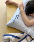 Person lying on a bed with a striped pillow and blanket featuring text.