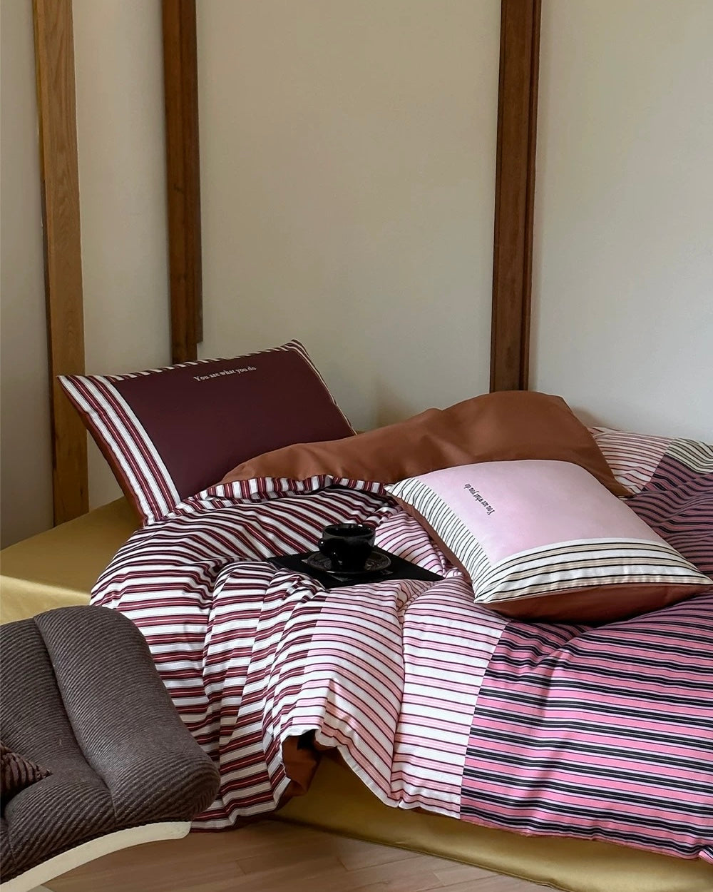 Bed with striped bedding and pillows against a plain wall