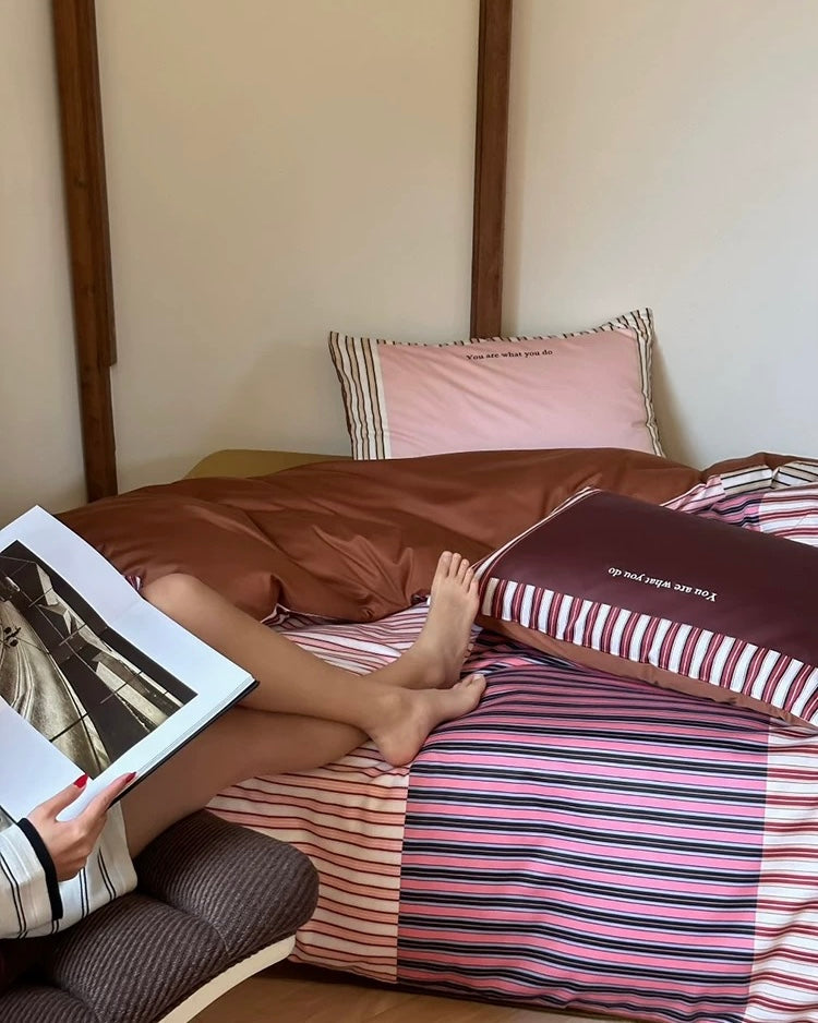 Person sitting on a bed holding a book, with striped bedding and a wooden headboard.
