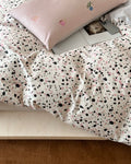 Person holding large pink embroidered pillowcase while wrapped in confetti dot duvet cover for cozy styling shot.