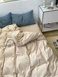 Unmade bed with beige comforter and blue pillows, nightstand with items in the background