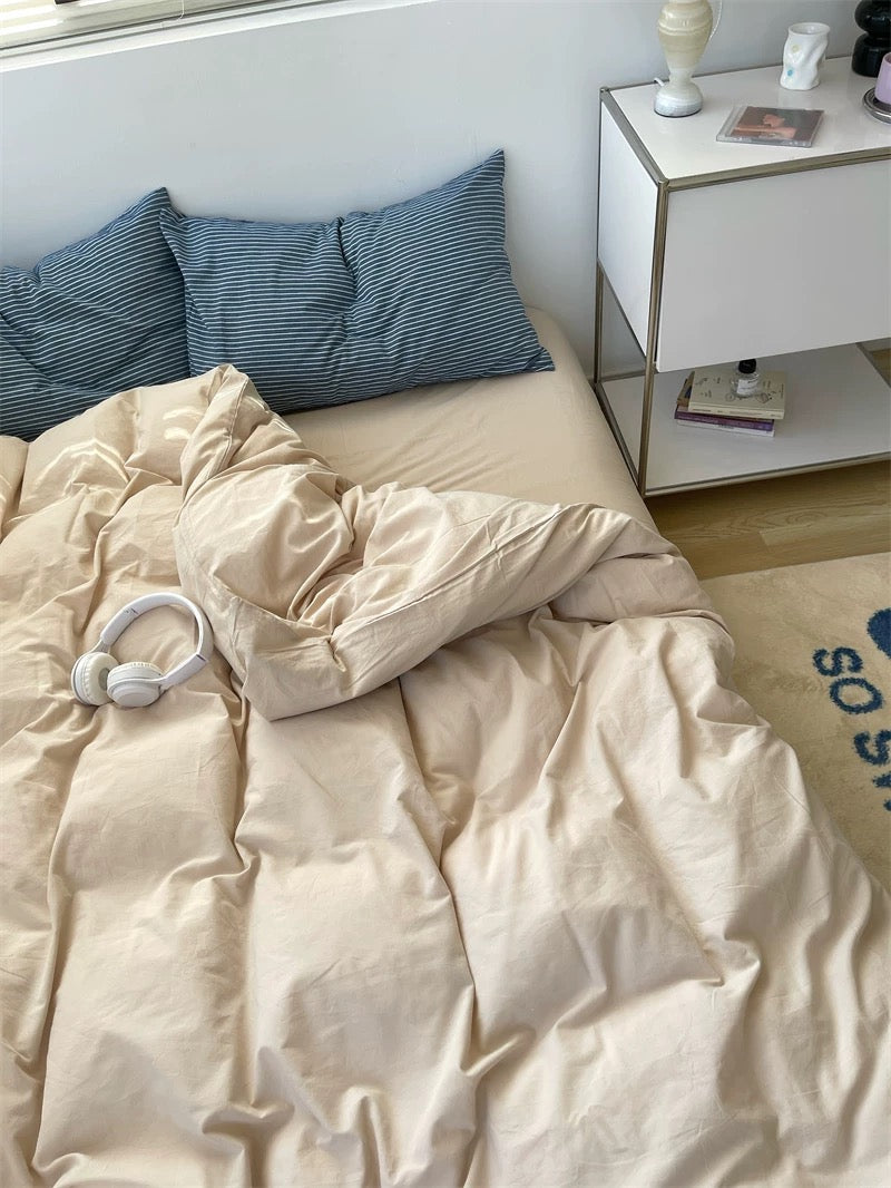 Unmade bed with beige comforter and blue pillows, nightstand with items in the background