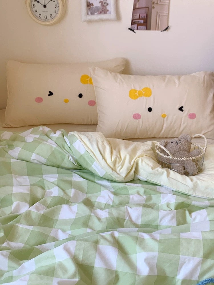 Bed with green and white checkered blanket, decorative pillows, and a teddy bear.