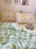 Bed with green checkered blanket, white pillows with smiley face design, and small basket on a light-colored wall background.