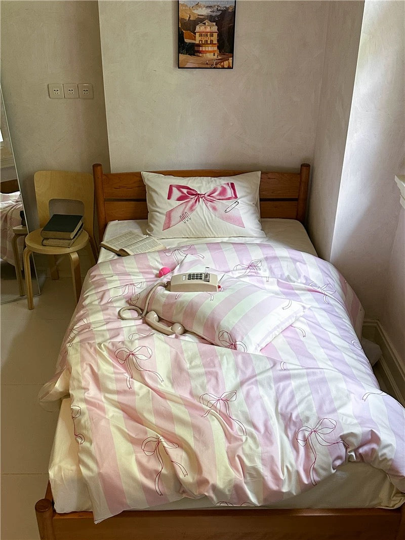 Bed with pink and white bedding in a room with a chair and wall art.