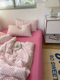 Bed with pink and white striped bedding and pillows, next to a nightstand with a lamp.