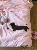Pink blanket with a black dog applique on a bed with a brown carpet.