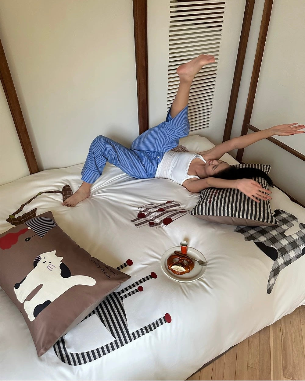 Person lying on a bed with a cat-themed pillow and a plate of food.