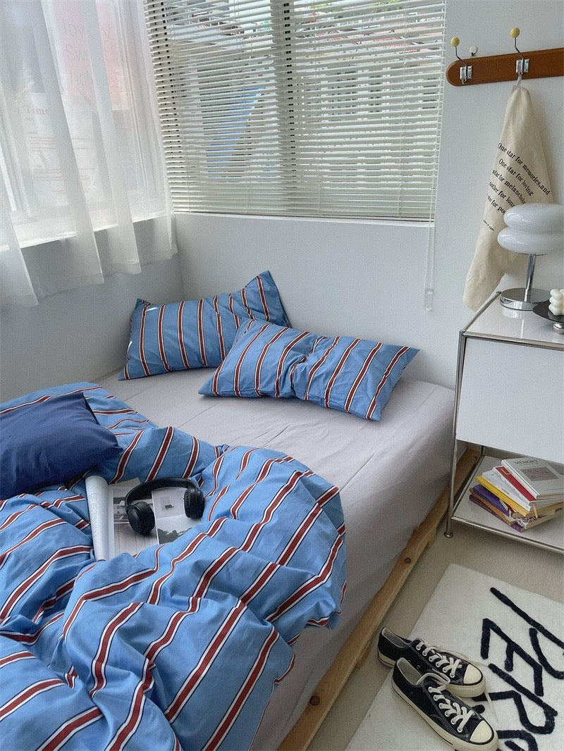 Bed with blue striped bedding in a room with white curtains and a nightstand.
