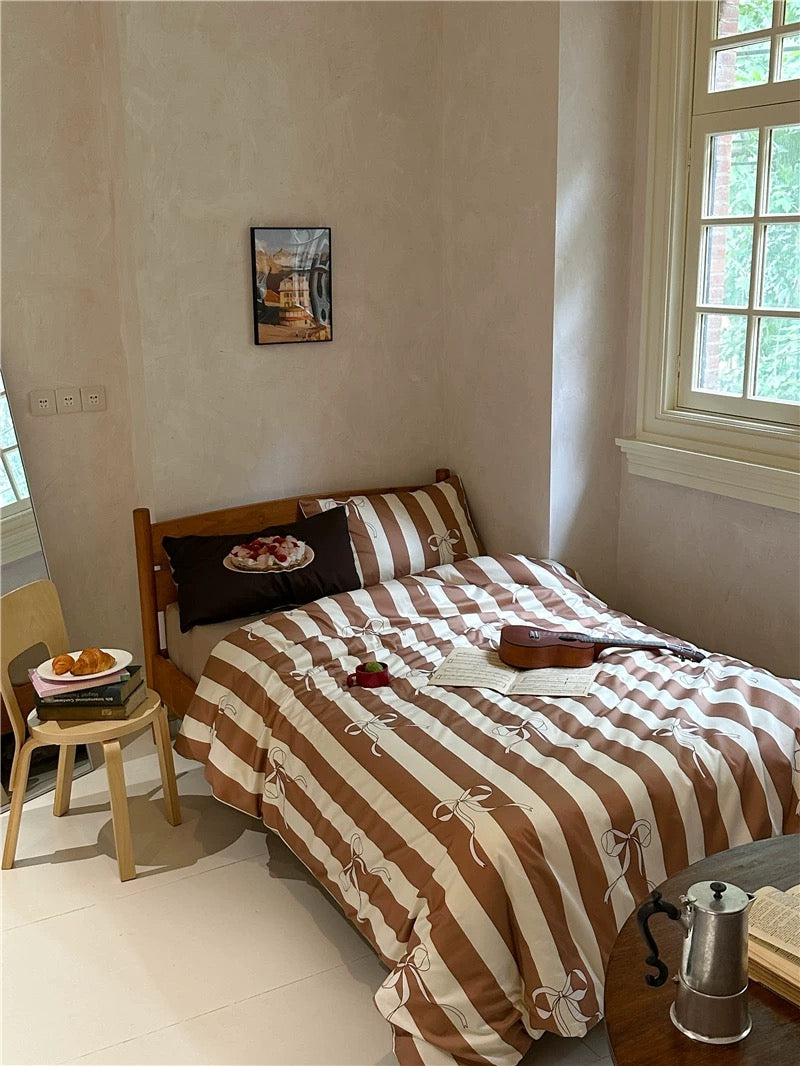 Bedroom with a bed covered in brown and beige striped bedding, pillows, and small table with food.