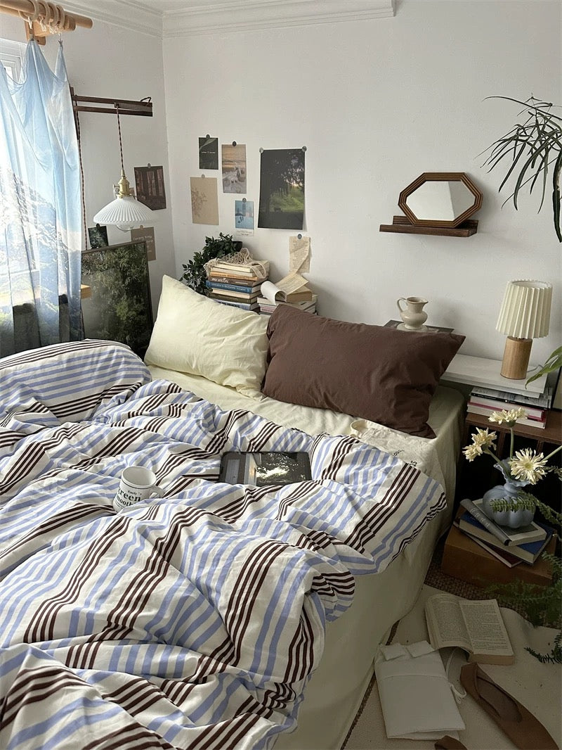 Bedroom with a bed, pillows, and a nightstand with books and a lamp.