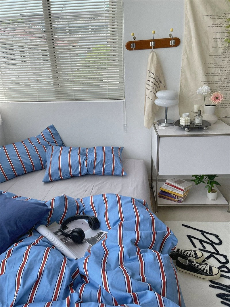 Bedroom with blue striped bedding, white nightstand, and window blinds.