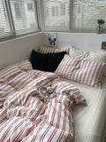 Bed with red and white striped bedding and pillows, near a window with blinds.