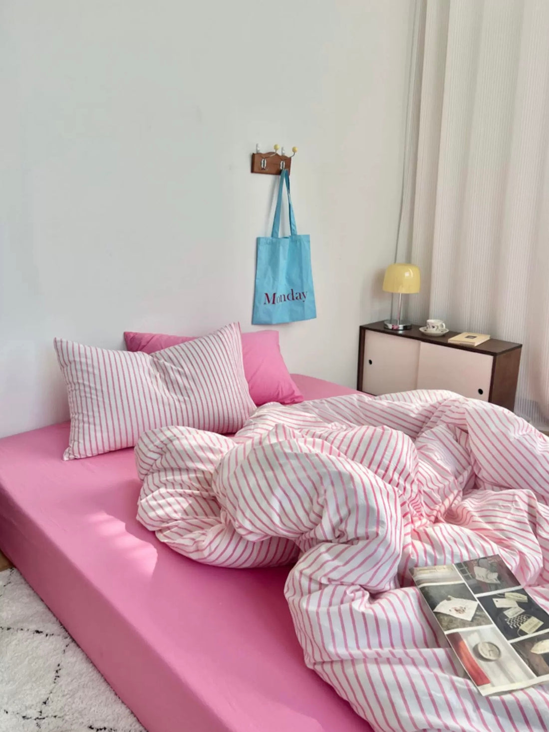 Pink bed with striped bedding in a room with a lamp and shelves.