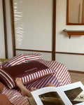 Person lying on a bed with striped bedding, reading a magazine.