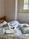 Bed with blue and white striped bedding, book, and snacks near a window.