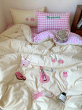 Bed with pink and white checkered pillow, embroidered design, and small teddy bear.