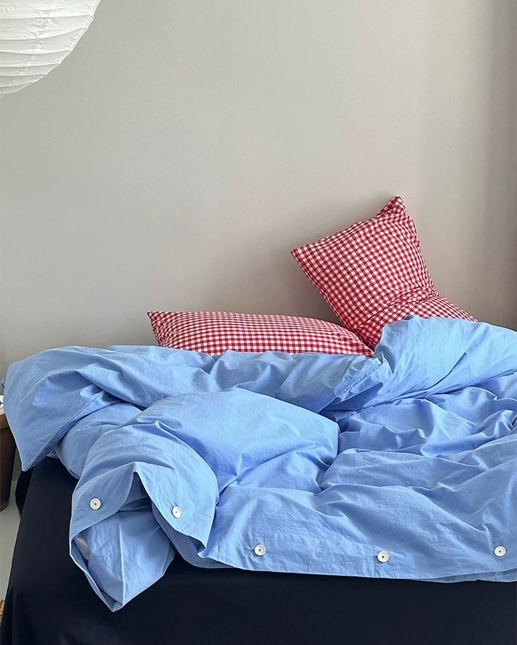 Minimalist bedding setup with blue cotton duvet and red plaid pillows
