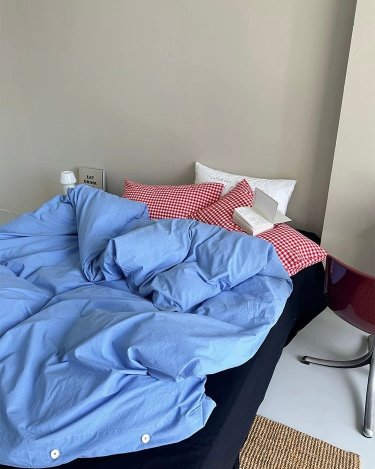 Blue cotton duvet cover with red plaid pillows on minimalist college bedroom bed