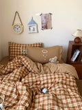 Bedroom with plaid comforter, pillows, and a teddy bear.