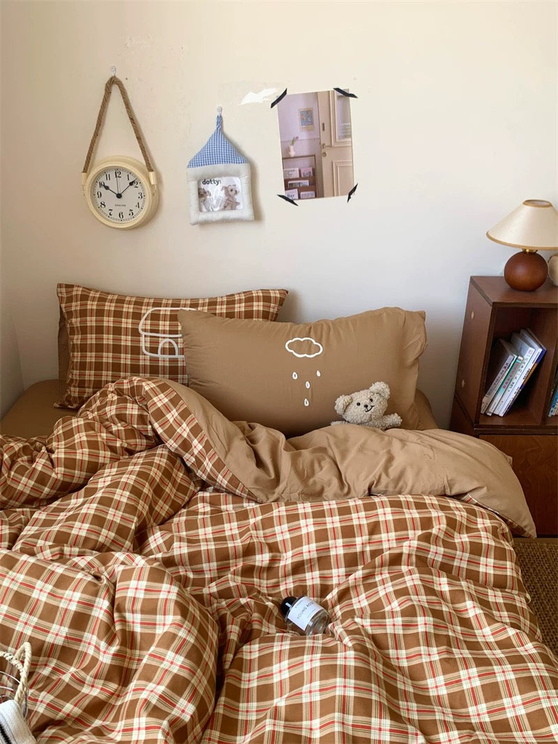 Bedroom with plaid comforter, pillows, and a teddy bear.