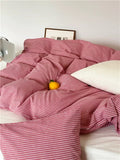 Pink striped comforter on a bed with a white pillow and yellow flower.
