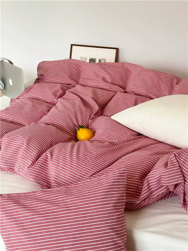Pink striped comforter on a bed with a white pillow and yellow flower.