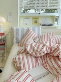 Striped red and white bedding on a bed with a Loewe shelf in the background.
