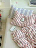 Bed with red and white striped bedding and a striped pillow, with a cup and book on the bed.