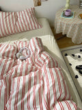 Bed with red and white striped bedding in a room with a small table and chair.