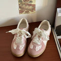Pink sneakers with white lace details on a wooden surface.